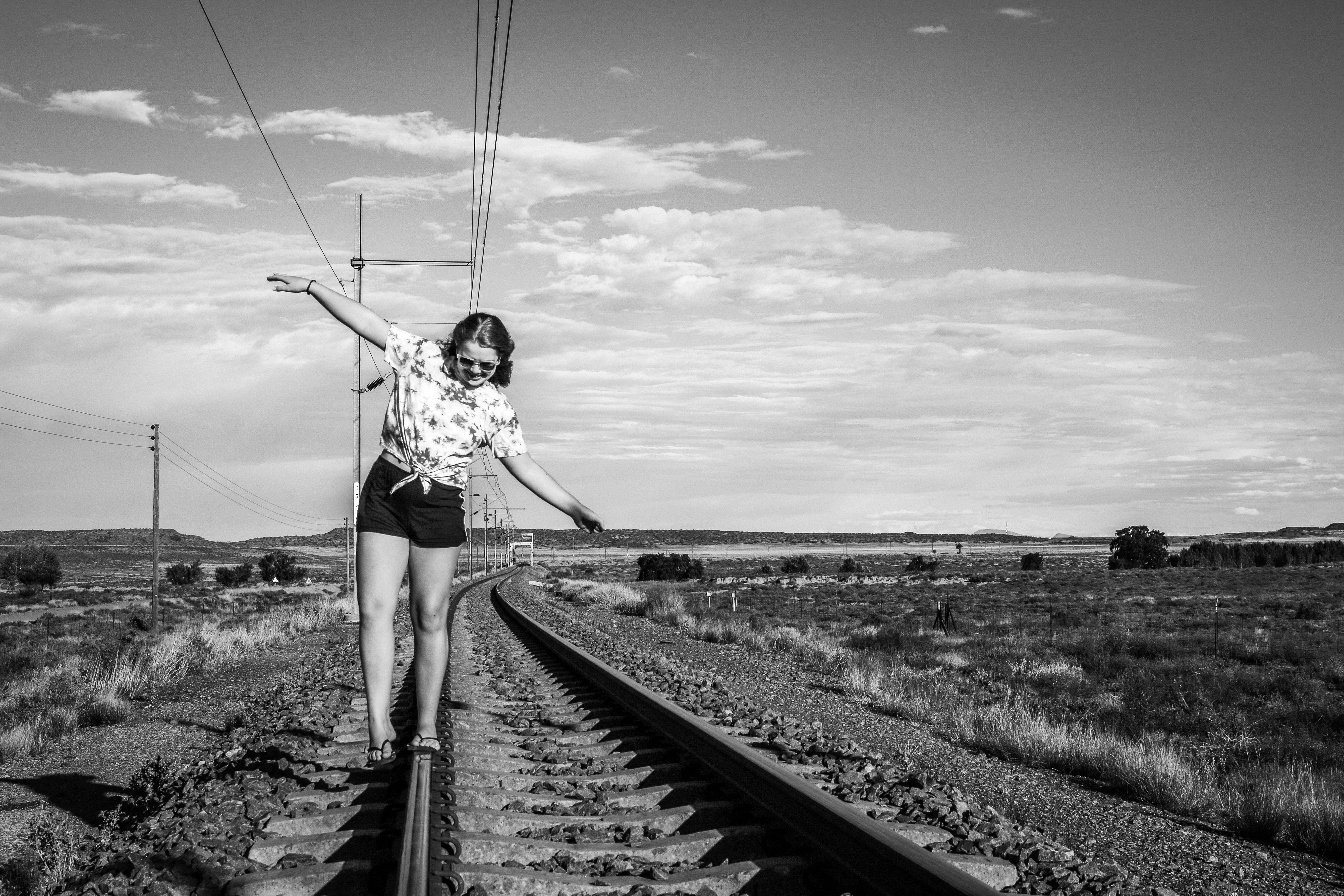 woman in white shirt and black shorts standing on train rail